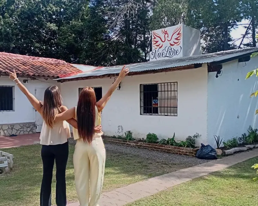 Dos compañeras celebrando con los brazos en alto frente a la casa de la comunidad
